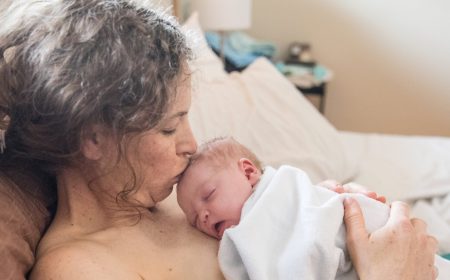 Postpartum mom kissing newborn baby's head while lying in bed