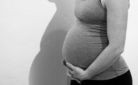 Black and white photo of pregnant mom with hands holding belly and pregnant shadow reflected on the wall